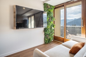 A modern living room with a mounted TV, a vertical garden, a sliding glass door leading to a balcony, and a sofa with a cushion. - L'Écrin des Aiguilles - Proche remontées mécanique (Fontcouverte-la-Toussuire)