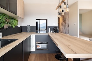 A modern kitchen with a built-in dishwasher, a coffee machine, and a view of mountains through a glass door. - L'Écrin des Aiguilles - Proche remontées mécanique (Fontcouverte-la-Toussuire)