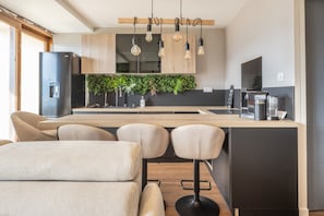 A modern kitchen with a wooden island, bar stools, a built-in herb garden, and a coffee machine. - L'Écrin des Aiguilles - Proche remontées mécanique (Fontcouverte-la-Toussuire)