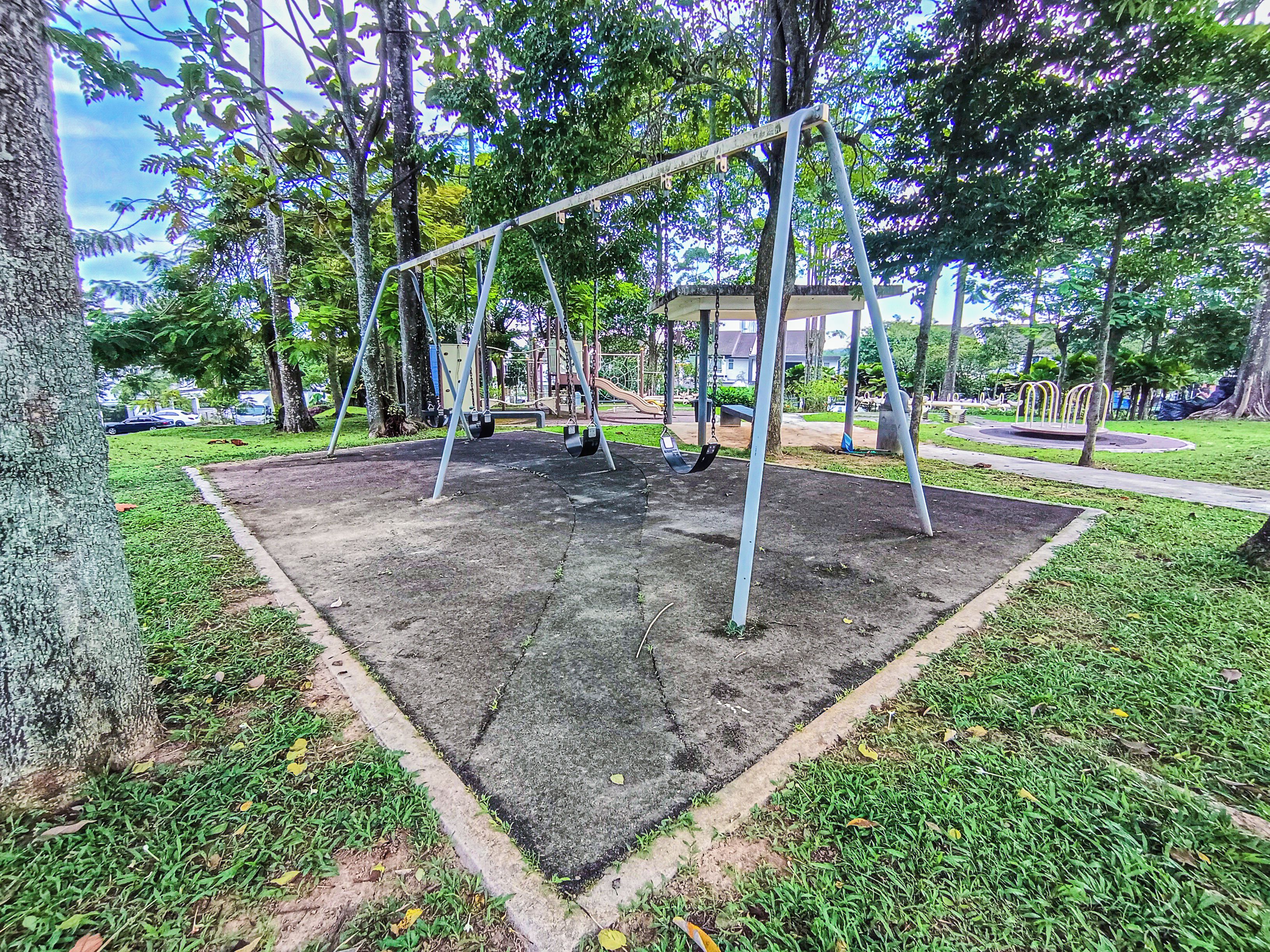 Un parc infantil amb cadiretes i tobogan, envoltat d'arbres i gespa.