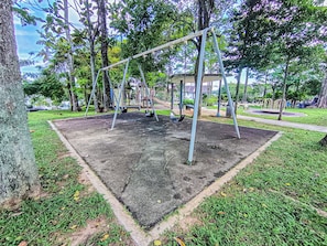A playground with swings and a slide, surrounded by trees and grass. - Modern Designer House BBQ Event by HCK (Puchong)