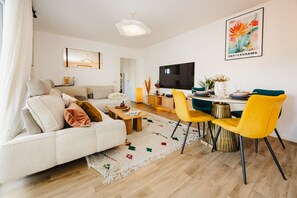 Un salon moderne avec un canapé, une table à manger et des chaises, un téléviseur à écran plat et un tableau accroché au mur.