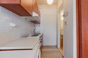 A compact kitchen with a stove, sink, and wooden cabinets. - Cozy Home Near The Sea 14 Studio with Sea View, Wi-Fi, and Air Conditioning (Ρέθυμνο)