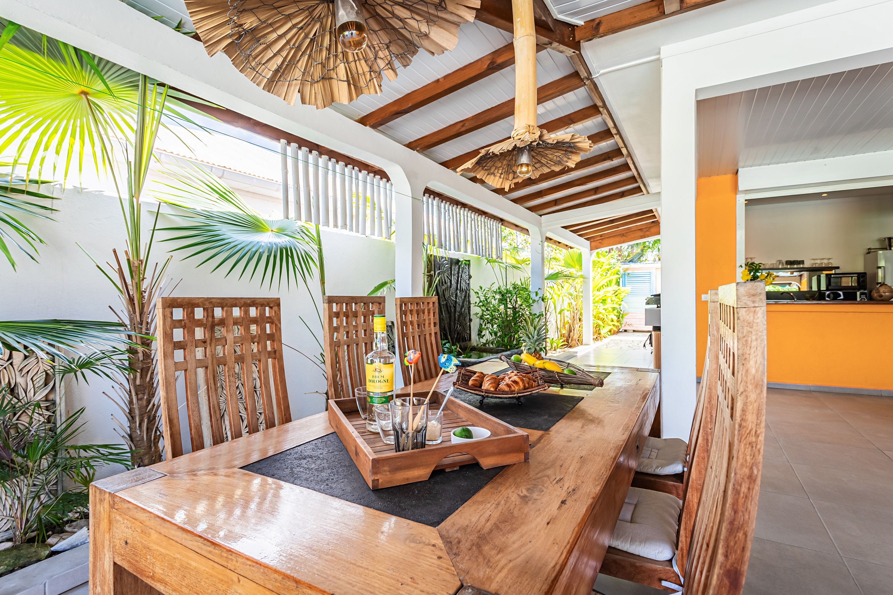 A wooden dining table with a bottle of rum, glasses, and a fruit basket.