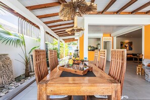 A wooden dining table with chairs, a bottle of alcohol, and glasses, set in a room with a high ceiling and wooden beams. - Villa La Saline - Piscine Privée (Saint-Francois)