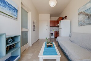 Ett kompakt bostadsutrymme med ett litet kök, en soffa, ett litet bord med en växt och en bokhylla.