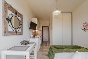 Une chambre à coucher comprenant un lit, un bureau, un miroir, une télévision et une porte donnant sur une salle de bain.