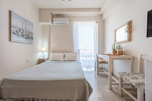 Ein Hotelzimmer mit Bett, Nachttisch, Lampe, Klimaanlage, einem Fenster mit Vorhängen und einem Wandbild.