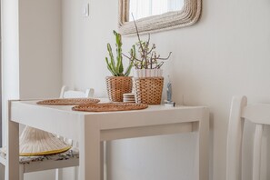 A white dining table with woven placemats, two potted plants, and a small decorative item. - Cozy Home Near The Sea 16 Studio with Balcony, Wi-Fi, and Air Conditioning (Ρέθυμνο)