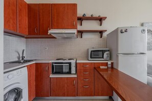 A kitchen with wooden cabinets, a microwave, a stove, a refrigerator, and a washing machine. - Cozy Home Near The Sea 16 Studio with Balcony, Wi-Fi, and Air Conditioning (Ρέθυμνο)