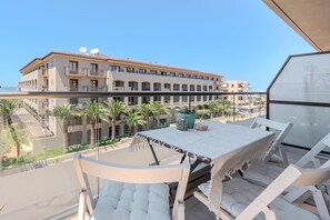 En balkon med et bord og stole, med udsigt over en bygning med flere balkoner og palmer.