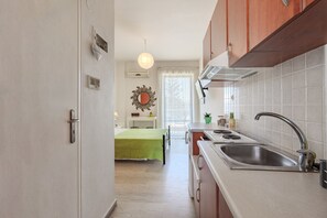 A kitchen with a sink, stove, and cabinets. There is a window with a curtain and a plant on the counter. - Cozy Home Near The Sea 17 Studio with Balcony, Wi-Fi, Air Conditioning (Ρέθυμνο)