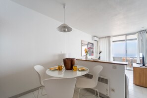 A modern kitchen with white cabinetry, a round dining table with white chairs, and a view of the sea through large windows. - Le Panorama de Cap-d'Ail - Climatisé, vue mer (Cap-d'Ail)