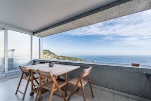 Een balkon met een tafel en stoelen, met uitzicht op een kustlandschap.