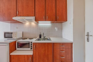 A compact kitchen with wooden cabinets, a microwave, a toaster, and a sink. - Cozy Home Near The Sea 18 Studio with Balcony, Wi-Fi, and Air Conditioning (Ρέθυμνο)