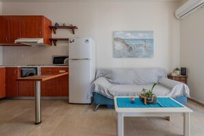 A compact living space with a kitchenette, a sofa, a coffee table, and a painting on the wall. - Cozy Home Near The Sea 19 Studio with Balcony, Wi-Fi, and Air Conditioning (Ρέθυμνο)