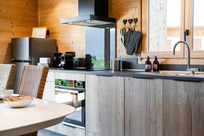 A modern kitchen with wooden cabinetry, a built-in oven, and a coffee machine. - Petit Chouda - Proche Télécabines (Saint-Chaffrey)