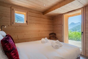 A wooden cabin bedroom with a bed, two windows, and a view of mountains. - Petit Chouda - Proche Télécabines (Saint-Chaffrey)