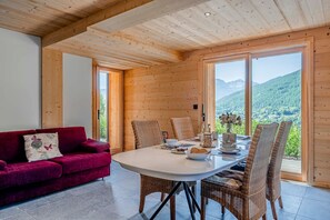 A cozy room with a wooden ceiling, a red sofa, a dining table with chairs, and a view of mountains through large windows. - Petit Chouda - Proche Télécabines (Saint-Chaffrey)