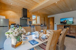 A modern kitchen with wooden beams, a dining area with wicker chairs, and a television on the wall. - Petit Chouda - Proche Télécabines (Saint-Chaffrey)