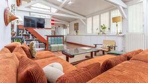 A spacious living room with a large sofa set, a glass coffee table, and a television. - Marais Saint Paul Atypique (Paris)
