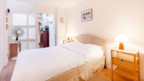 Een slaapkamer met een bed, nachtkastjes, een lamp, een ventilator en een schilderij aan de muur.