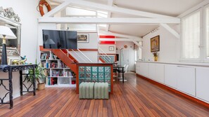 Een ruime kamer met houten vloer, een wenteltrap, een boekenkast en een televisie.