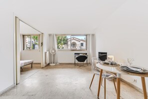 Una habitació àmplia amb zona de menjador, un llit i vista a un edifici amb balcó.
