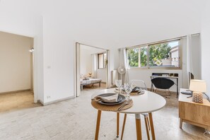 Une pièce moderne et bien éclairée, comprenant un coin repas, un lit et une fenêtre donnant sur un paysage verdoyant.