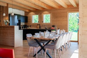 Cuina moderna amb parets de fusta, zona de menjador amb taula i caires de fusta, i vista a la vegetació exterior.