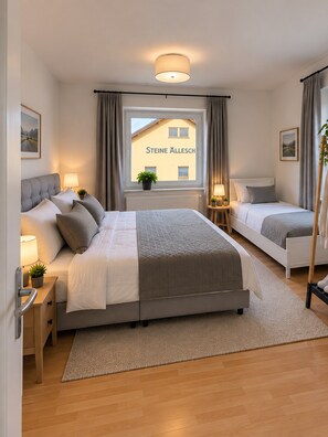 A modern bedroom with a large bed, two bedside tables, a window with curtains, and a view of a building outside. - Ferienwohnung 'Felix Living 13 – Lusenblick - 3 Schlafzimmer & 3 Bäder' (Mauth)