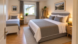 Ein Hotelzimmer mit einem großen Bett, einem kleineren Bett, einem Fenster mit Vorhängen, einer Pflanze und einem Gemälde an der Wand.