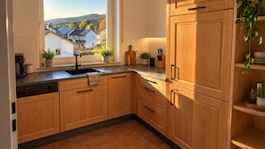 A kitchen with wooden cabinets, a black sink, and a window overlooking a residential area. - Ferienwohnung 'Felix Living 13 – Lusenblick - 3 Schlafzimmer & 3 Bäder' (Mauth)