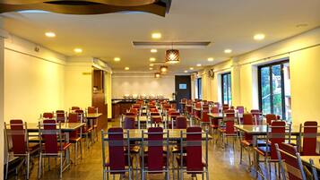 Uma sala de jantar ampla, com várias mesas e cadeiras, um buffet e grandes janelas que oferecem luz natural.