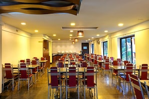 A spacious dining area with multiple tables and chairs, a buffet counter, and large windows providing natural light. - Varaha Valley (Kodaikanal)