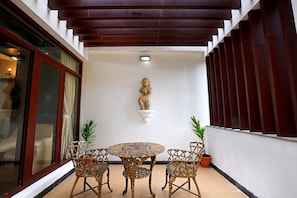 A covered patio area with a round table and two chairs, a wall-mounted sculpture, and potted plants. - Varaha Valley (Kodaikanal)