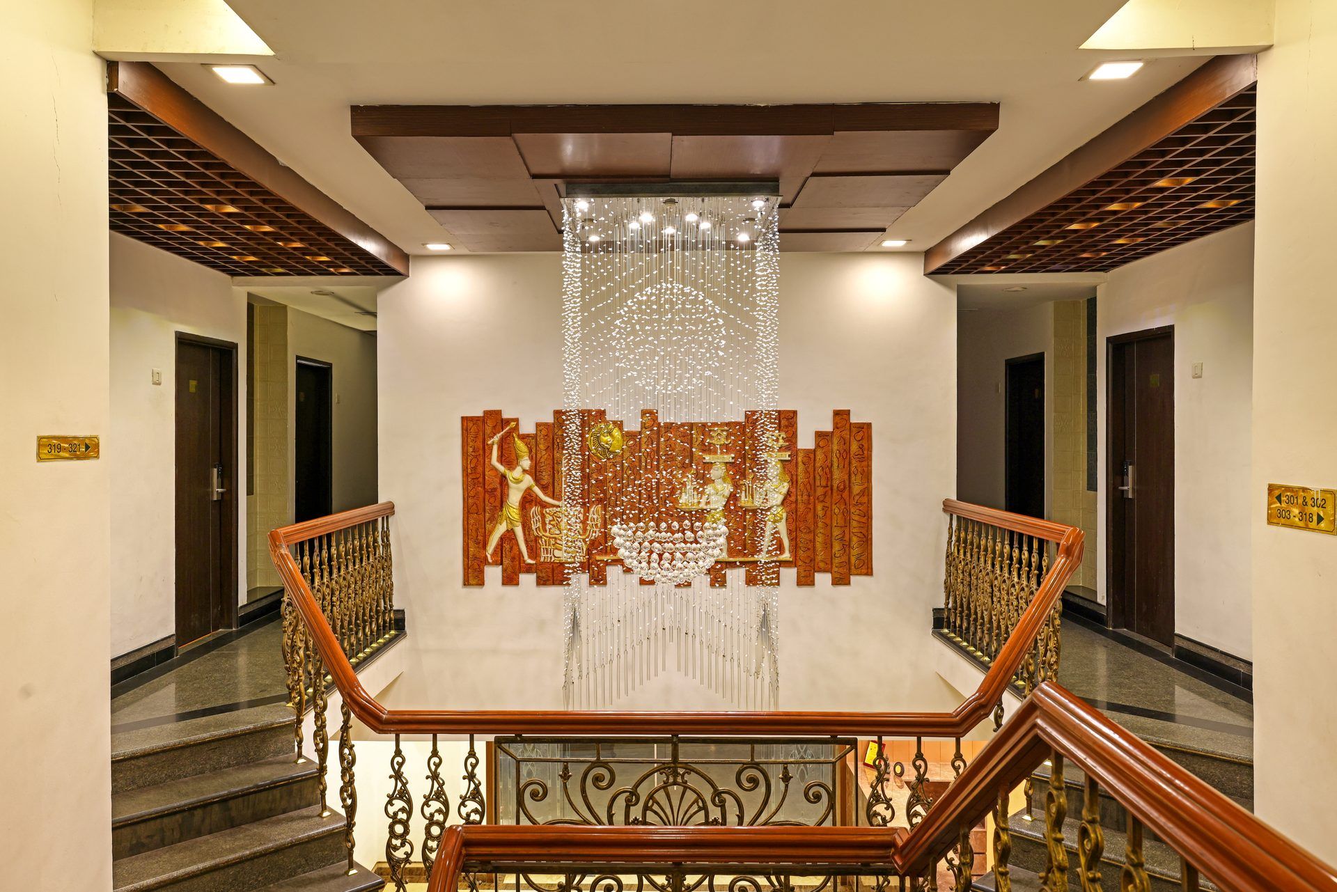 Una escalera con barandillas ornamentales, un muro decorativo con una figura y un aplique colgante.