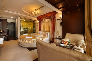 A luxurious bedroom with a round bed, a sitting area with a chair and a small table, and a glass-enclosed shower area. - Varaha Valley (Kodaikanal)