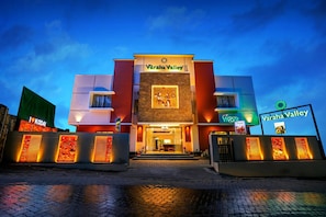 A Varaha Valley hotel with a modern facade, a central entrance, and illuminated signage. - Varaha Valley (Kodaikanal)