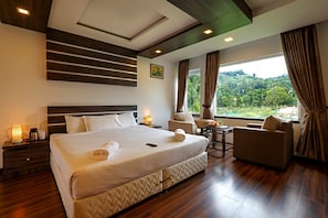 Habitación de hotel con una cama grande, zona de estar y vistas al exterior.
