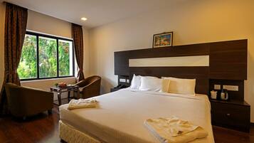 Quarto de hotel com uma cama grande, uma escrivaninha, uma cadeira e uma janela com cortinas.