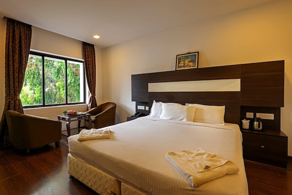 A hotel room with a large bed, a desk, a chair, and a window with curtains. - Varaha Valley (Kodaikanal)