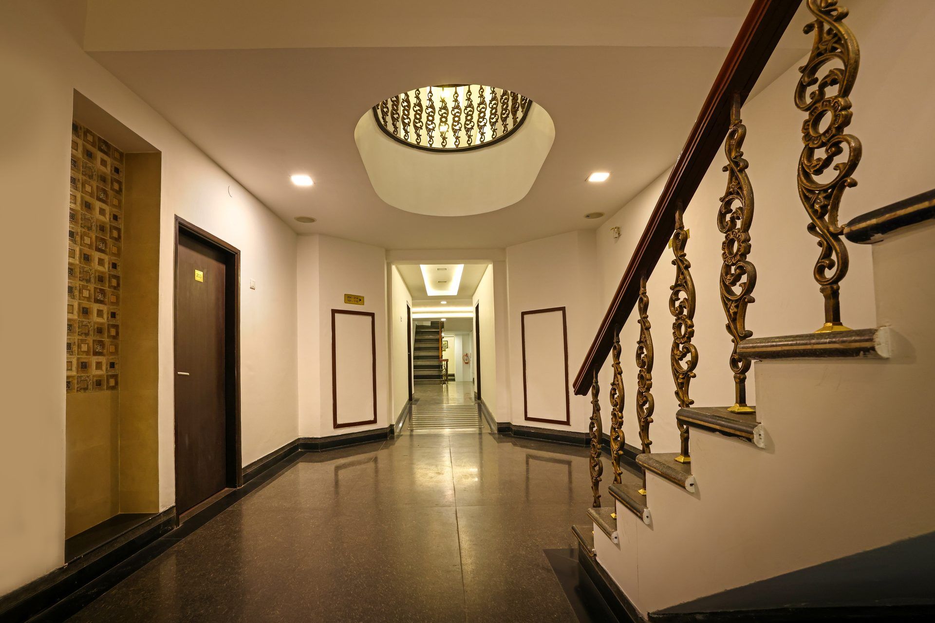 A hotel hallway with a polished floor, a grand staircase with ornate metal railings, and a decorative ceiling light fixture.