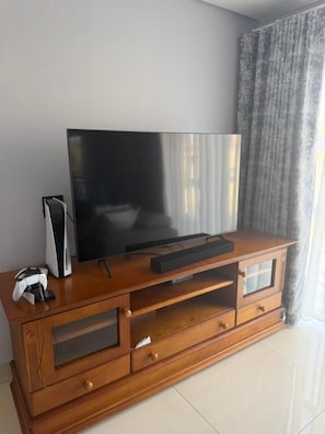 Un mueble de madera con un televisor de pantalla plana, una consola de videojuegos y un control remoto.