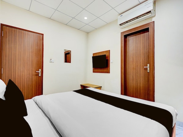 A hotel room with a bed, a small table, a TV mounted on the wall, and two wooden doors. - Classic Hotel Shivalika (Jaipur)