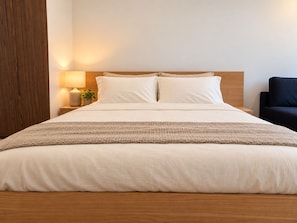 A neatly made bed with a wooden headboard, a bedside lamp, and a small plant on the nightstand. - Heart of Flagstaff Gardens & QV Market Balcony (Melbourne)