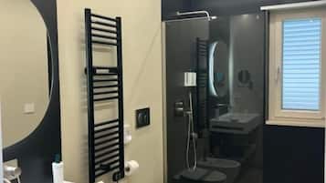 Un baño moderno con un lavamanos blanco, un toallero negro, una cabina de ducha con mampara de vidrio y un inodoro.