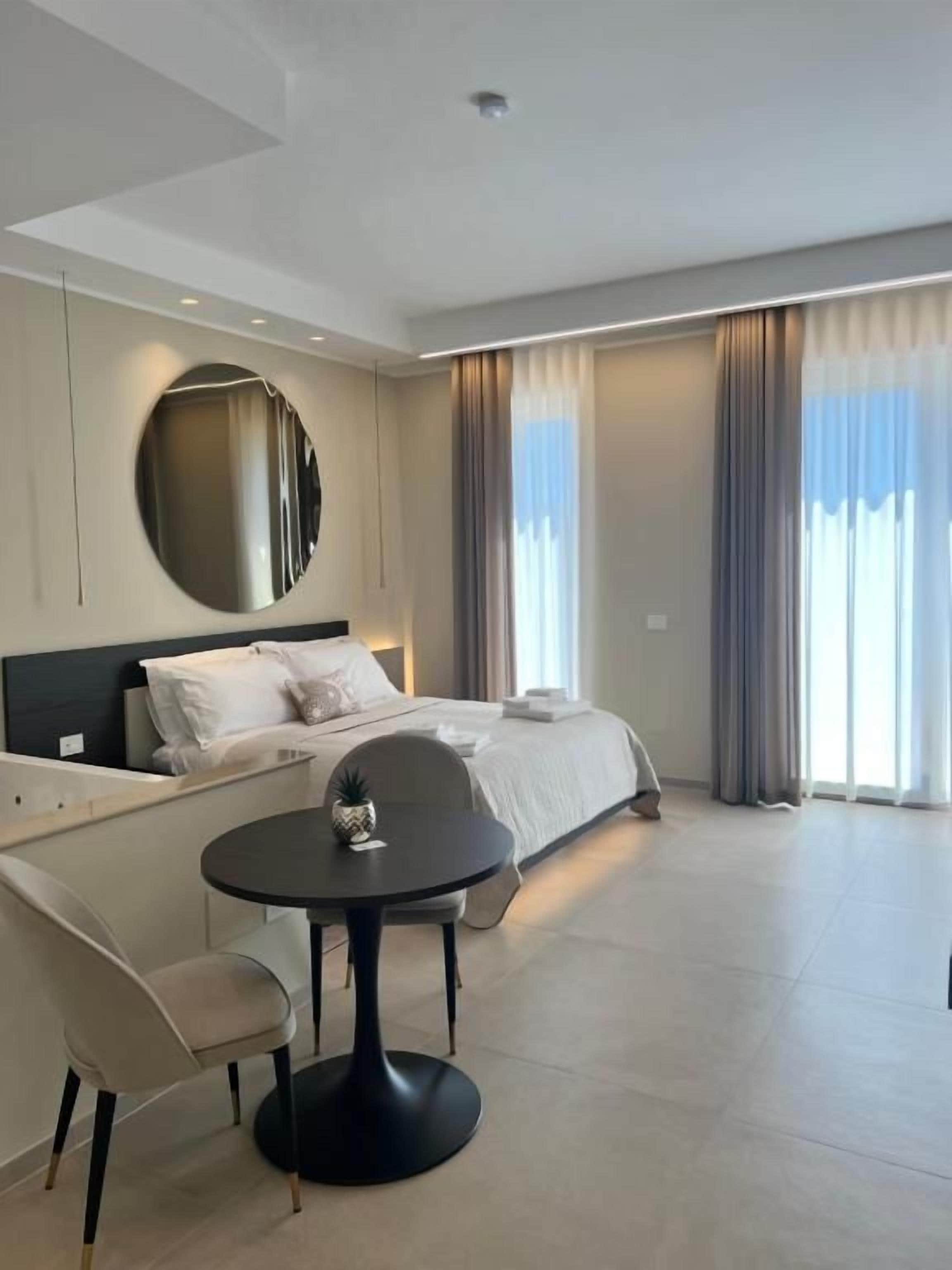 Una habitación de hotel moderna con una cama, un espejo redondo, una mesita pequeña y una silla.