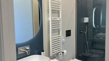 Een moderne badkamer met een grote spiegel, een wit wastafelmeubel, een hygiëneschuimer en een douche met glazen wanden.