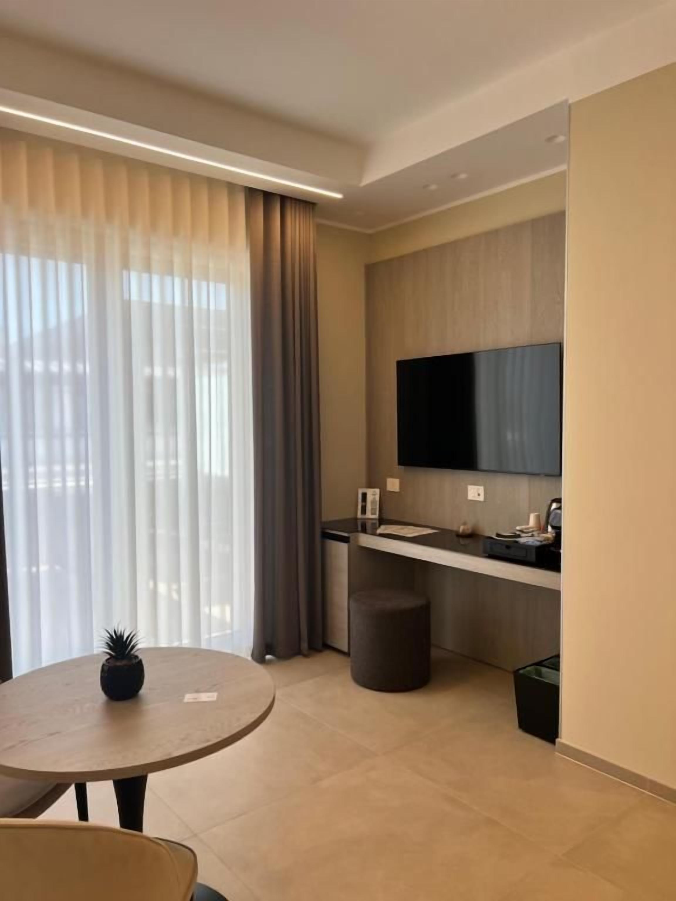 Une chambre d’hôtel moderne avec une table ronde, une petite plante en pot, un canapé, un téléviseur à écran plat fixé au mur et un coin cuisine.